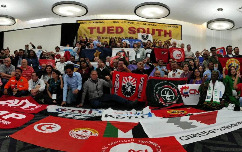 People gathered for a photo. They have their fists up in the air and are surrounded by lots of flags. 