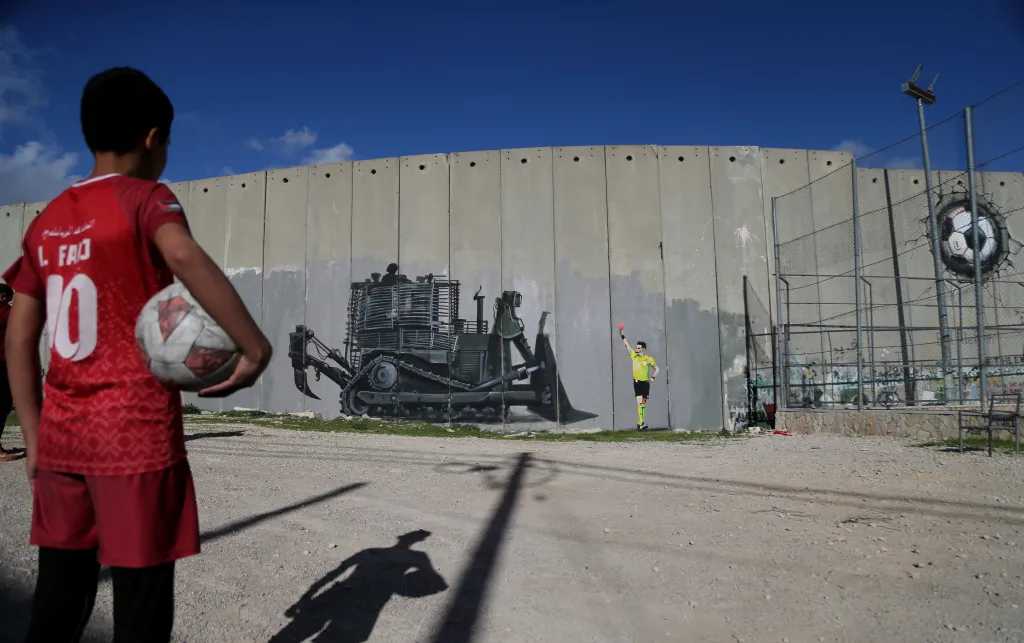 Boy holds football and looks at graffiti 