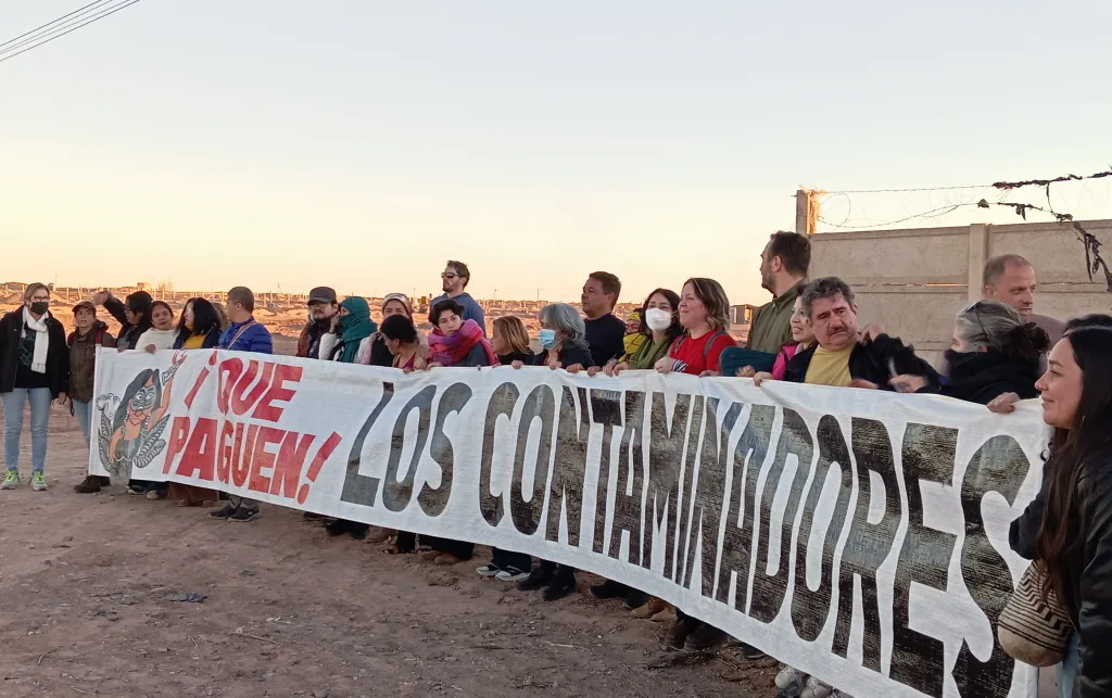 People at a protest holding a big 'Make Polluters Pay' sign in Spanish.